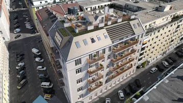 Luftaufnahme eines modernen Wohngebäudes mit Dachterrassen und Balkonen in städtischer Umgebung.