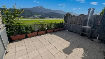 Geräumige Terrasse mit Bergblick, Grillplatz und Pflanzkübeln unter blauem Himmel.