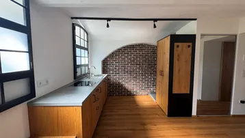 Moderne Küche mit Holzelementen, Backsteinwand und großen Fenstern, die viel Licht hereinlassen.