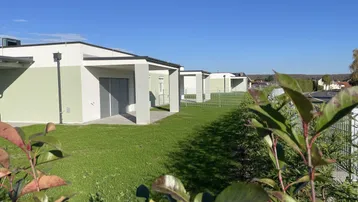 Reihe moderner Neubauten mit grünen Fassaden und gepflegten Rasenflächen unter blauem Himmel.