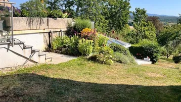 Weitläufiger Garten mit Rasenfläche, vielfältiger Bepflanzung und Fernblick auf die Landschaft.