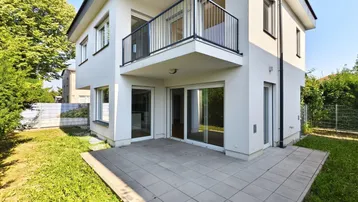 Moderne Hausfassade mit weißem Putz, großer Terrasse und kleinem Gartenbereich.