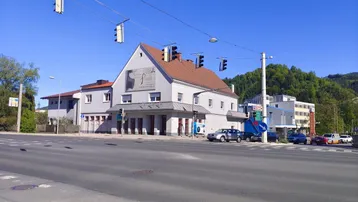 Gebäudeansicht von der Straße mit umliegender Bebauung und klarem blauen Himmel.