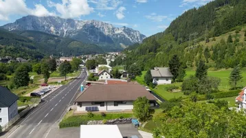 Weitläufige Ansicht einer Ortschaft mit Straße, Häusern und majestätischer Bergkulisse.