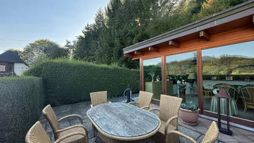 Möblierte Terrasse mit Rattanmöbeln, umgeben von einer Hecke und Blick auf die Natur.