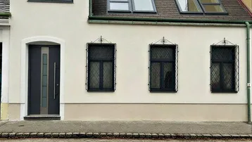 Die helle Fassade des Hauses mit Eingangstür und Dachfenstern zur Straße hin.