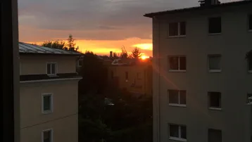Sonnenuntergang zwischen Wohngebäuden mit Blick auf die Straße und parkende Autos.