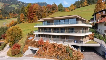 Modernes Apartmentgebäude mit begrüntem Dach und Balkonen in alpiner Hanglage.