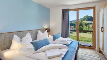Helles Schlafzimmer mit Doppelbett, blauer Akzentwand und Bergblick.