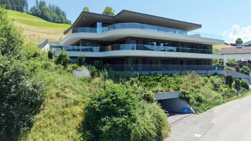 Modernes Mehrfamilienhaus mit geschwungenen Balkonen und Tiefgaragenzufahrt in grüner Hanglage.