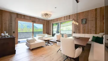 Helles Wohn- und Esszimmer mit Holzwänden, Parkettboden und Zugang zur Terrasse mit Bergblick.