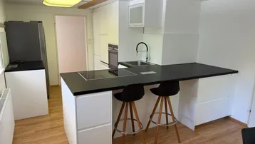 Moderne Küche mit schwarzer Arbeitsplatte, Kochinsel und Holzbalken an der Decke.