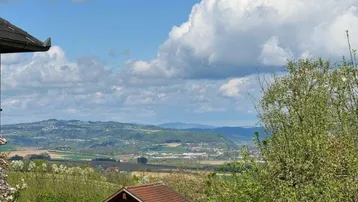 Weitläufiger Blick über die grüne Landschaft und Hügel unter bewölktem Himmel.