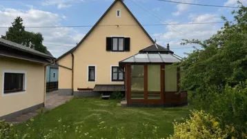 Traditionelles Haus mit gelber Fassade, großem Garten, Rasenfläche und einem charmanten Wintergarten.