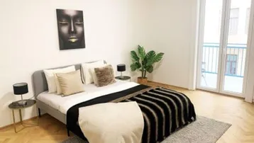 Helles Schlafzimmer mit Doppelbett, Fischgrätparkett und Zugang zu einem französischen Balkon.