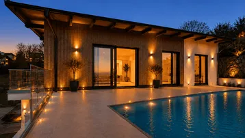 Moderne Villa bei Sonnenuntergang mit beleuchteter Holzfassade, großem Pool und Panoramablick.