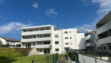 Moderne Wohnanlage mit mehreren Gebäuden, Balkonen und gepflegten Grünflächen unter blauem Himmel.