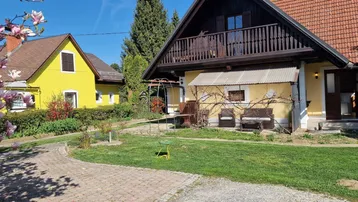 Ländliches Haus mit gelber Fassade, Holzbalkon und blühenden Magnolien im Vorgarten.