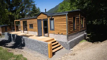 Modernes Holzhaus mit großer Holzterrasse und Gabionenmauern in natürlicher Umgebung.
