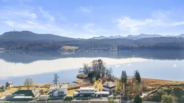 Panoramablick auf den See mit umliegenden Bergen und Häusern am Ufer unter blauem Himmel.