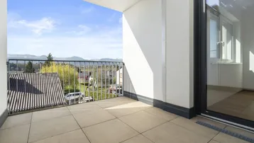 Heller Balkon mit Fliesenboden und weitem Blick auf die umliegende Landschaft und Berge.