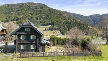 Charmantes Holzhaus mit grünen Fensterläden und Blick auf die umliegende Berglandschaft.
