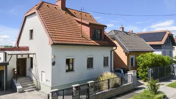 Vorderansicht eines Einfamilienhauses mit Satteldach, Vorgarten und gepflegter Fassade unter blauem Himmel.