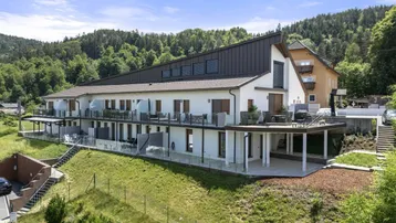Modernes Mehrfamilienhaus mit mehreren Balkonen und Terrassen in grüner Hanglage.