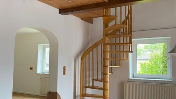 Heller Wohnbereich mit Holzdecken, sichtbaren Balken und einer eleganten Wendeltreppe.