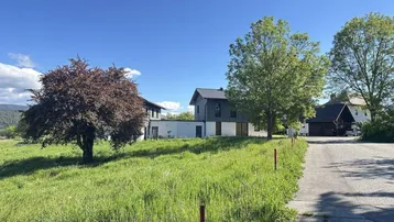 Modernes Haus mit Holzfassade und großem Gartenbereich unter blauem Himmel.