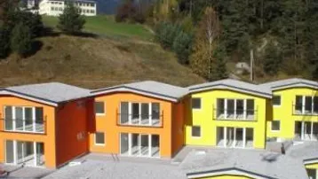 Reihenhäuser mit farbigen Fassaden vor einer beeindruckenden Bergkulisse und Wald.