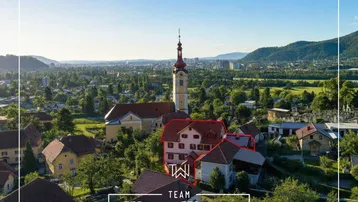 Luftaufnahme eines historischen Gebäudes mit Kirche und Bergblick in einer malerischen Stadt.