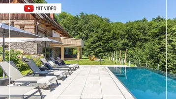 Luxuriöser Außenbereich mit Infinity-Pool, Liegestühlen und Blick auf die grüne Landschaft.