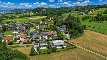 Panoramablick aus der Vogelperspektive auf eine idyllische Wohnsiedlung in grüner Hügellandschaft.