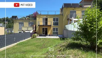 Gelbes Mehrfamilienhaus mit Garten, Balkonen, Dachterrassen und Solaranlagen unter blauem Himmel.