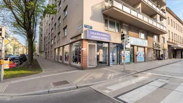 Außenansicht des Gebäudes an einer Straßenecke mit einem Geschäft im Erdgeschoss und Balkonen in den oberen Etagen.