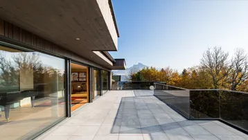 Geräumige Terrasse mit Fliesenboden, Glasgeländer und weitem Blick auf die Berge und den See.