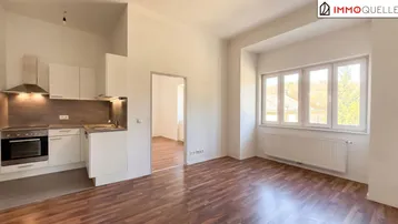 Heller offener Wohnbereich mit integrierter Küche, Parkettboden und großen Fenstern.