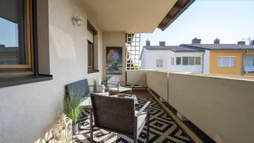 Sonniger Balkon mit bequemen Sitzmöbeln und Blick auf die umliegenden Häuser.