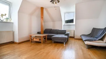 Helles Wohnzimmer mit Dachschrägen, Holzfußboden, modernem Sofa und Deckenventilator.