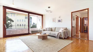 Helles Wohnzimmer mit Parkettboden, beigem Sofa und Zugang zu einem Balkon.