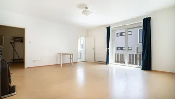 Helles Wohnzimmer mit Parkettboden, Kachelofen und Zugang zum Balkon.