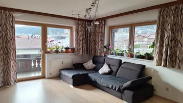 Helles Wohnzimmer mit gemütlichem Sofa, Holzboden und Zugang zum Balkon mit Bergblick.