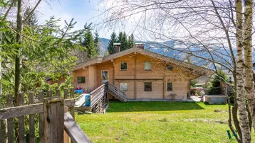 Charmantes Holzhaus in ländlicher Umgebung mit Blick auf die Berge und viel Grün unter strahlendem Himmel.