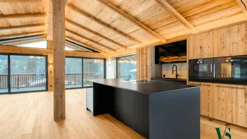 Modernes Wohnzimmer mit offener Küche, Holzbalkendecke und großen Panoramafenstern mit Bergblick.