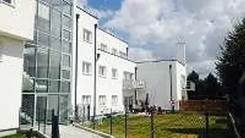 Modernes weißes Gebäude mit Glasfassadenaufzug und gepflegter Rasenfläche im Außenbereich.