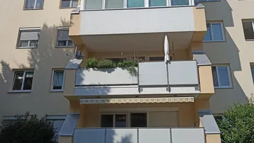 Fassade eines Mehrfamilienhauses mit mehreren Balkonen, Markisen und gepflegten Grünflächen.