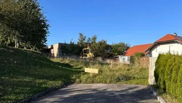 Unbebautes Grundstück mit Zufahrtsweg und Blick auf umliegende Wohnhäuser.