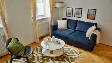 Helles Wohnzimmer mit bequemem blauen Sofa, Couchtisch und klassischem Fischgrätparkettboden.