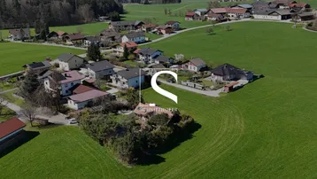 Luftaufnahme einer ländlichen Wohnsiedlung umgeben von weiten grünen Feldern und Wäldern.